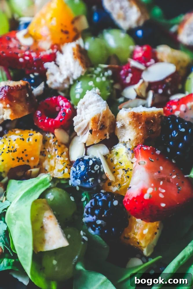 Picture of spinach salad with grapes, strawberries, blackberries, blueberries, raspberries, chicken, poppy seeds, hemp hearts, and a citrus poppyseed dressing on a black plate. 