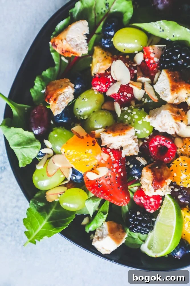 Picture of spinach salad with grapes, strawberries, blackberries, blueberries, raspberries, chicken, poppy seeds, hemp hearts, and a citrus poppyseed dressing on a black plate. 