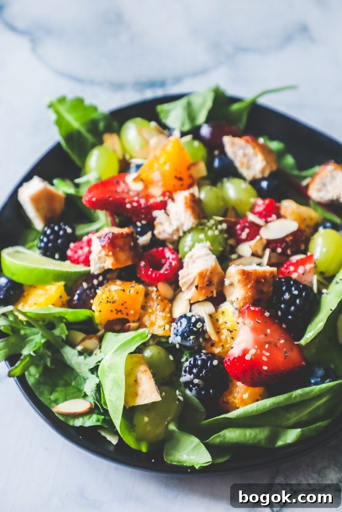 Picture of spinach salad with grapes, strawberries, blackberries, blueberries, raspberries, chicken, poppy seeds, hemp hearts, and a citrus poppyseed dressing on a black plate. 