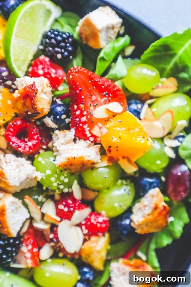 Picture of spinach salad with grapes, strawberries, blackberries, blueberries, raspberries, chicken, poppy seeds, hemp hearts, and a citrus poppyseed dressing on a black plate. 