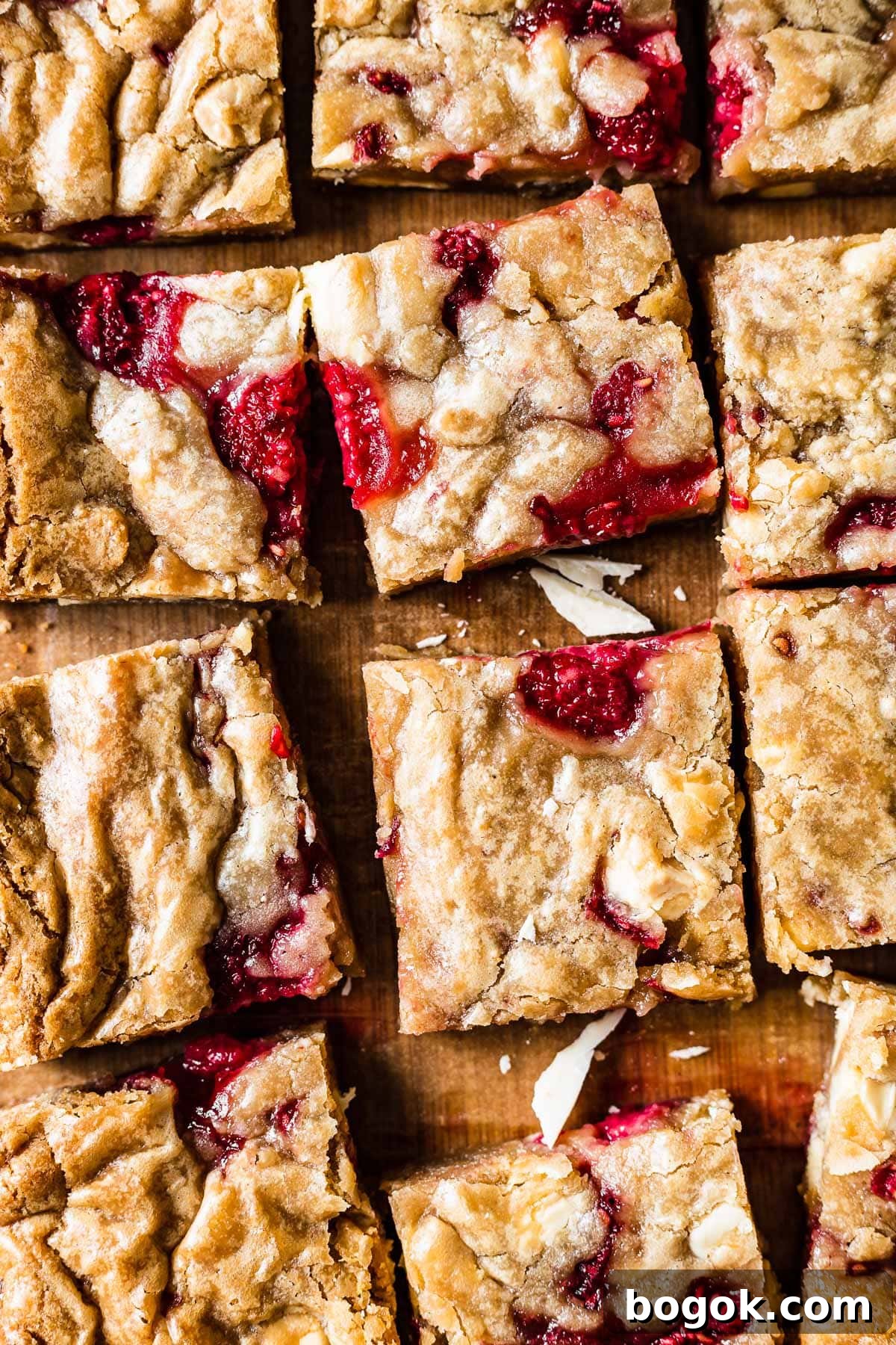 Raspberry White Chocolate Blondies Recipe with Crispy Edges 2 Squares of blondies studded with raspberries and white chocolate on a wooden cutting board.