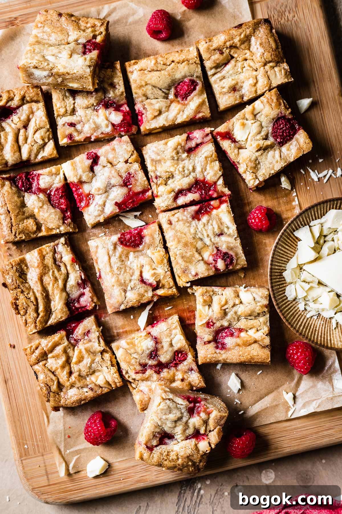 Raspberry White Chocolate Blondies Recipe with Crispy Edges 12 Raspberry white chocolate blondie squares on a wooden cutting board.