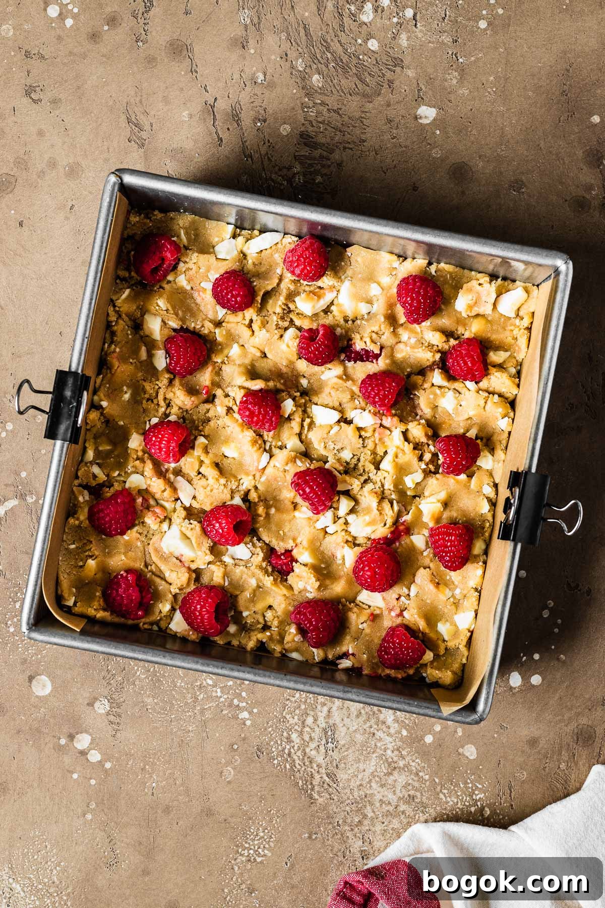Raspberry White Chocolate Blondies Recipe with Crispy Edges 8 A square pan with unbaked blondie dough studded with white chocolate and raspberries.