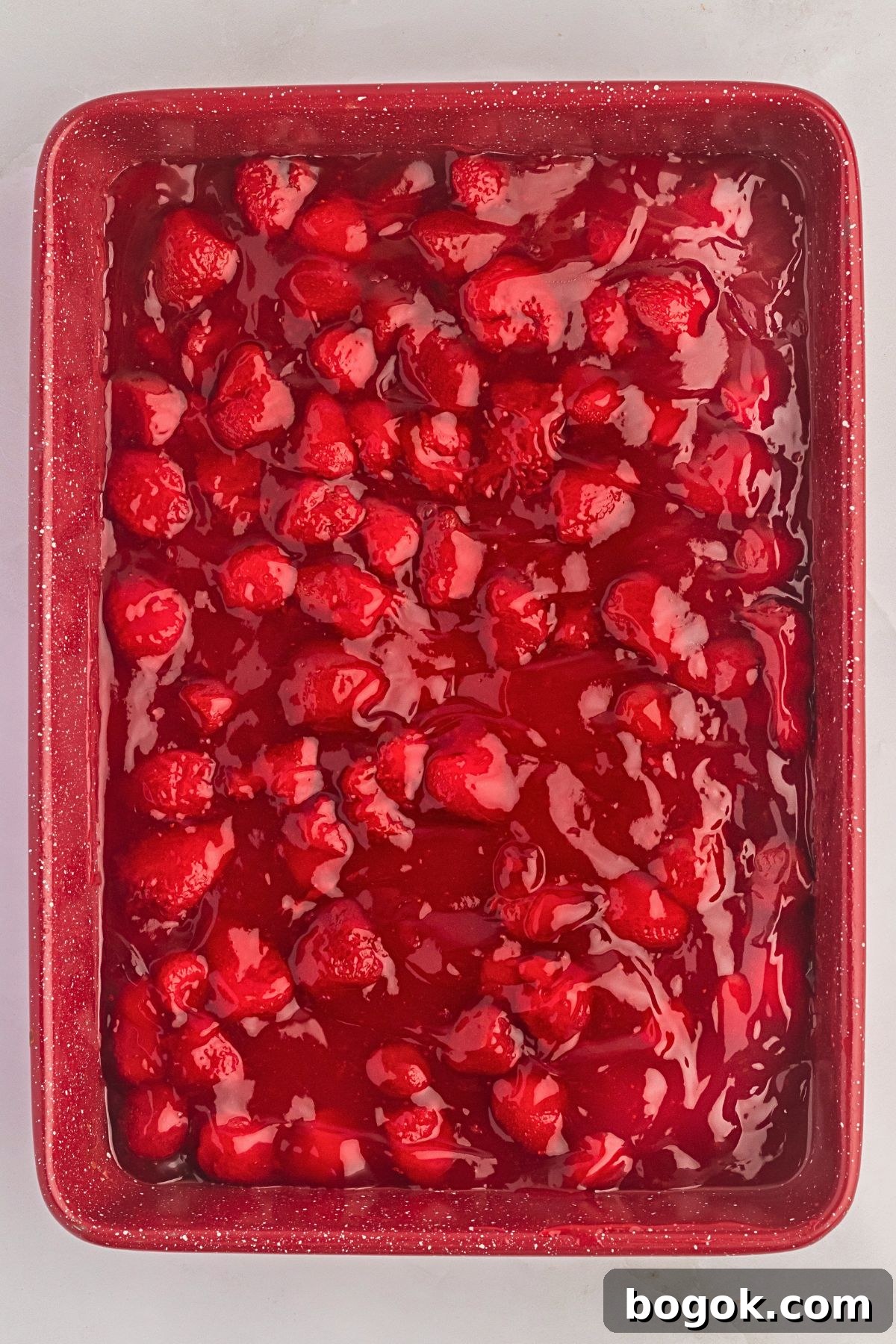 Strawberry pie filling poured into cake pan. 