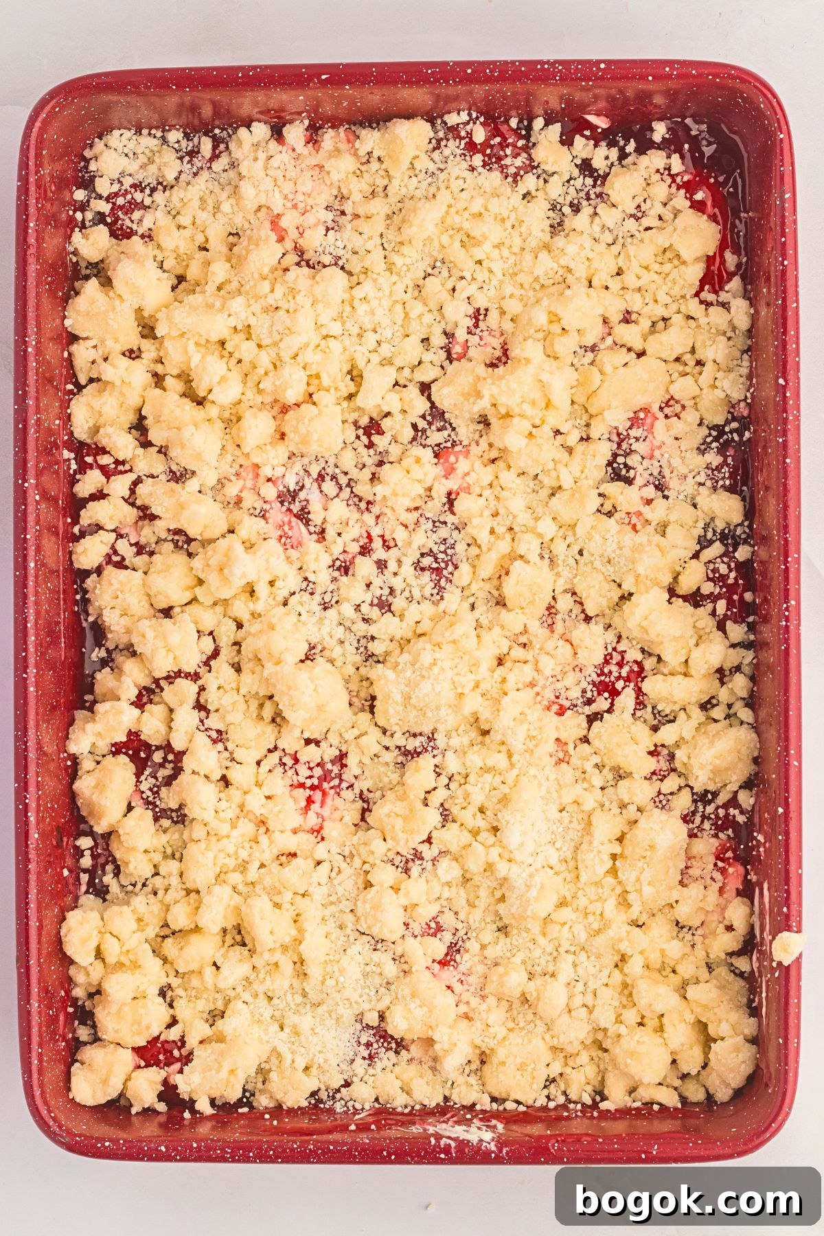 Uncooked cake mix mixed with butter dolloped on top a strawberry pie filling. 