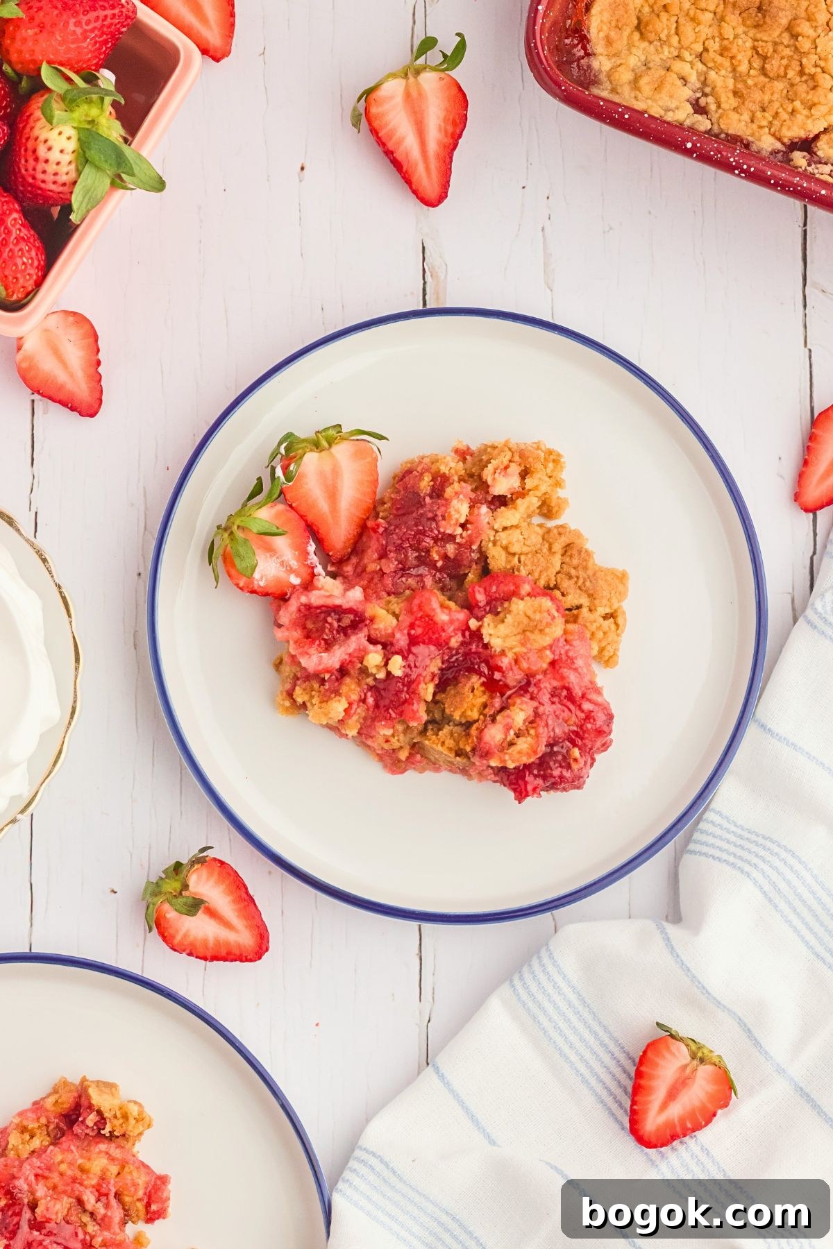 Strawberry dump cake on a white plate with strawberry slices scattered around the plate. 