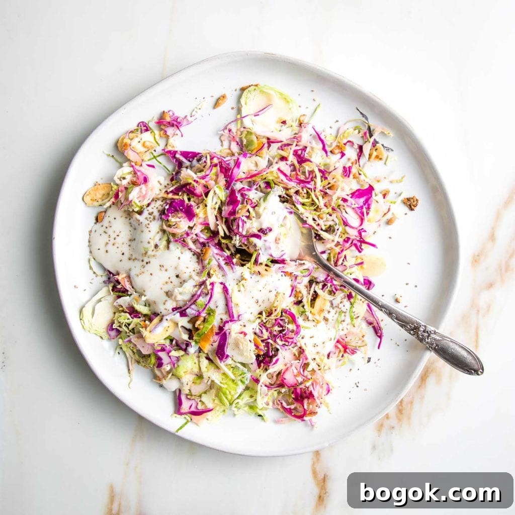 White plate with shredded brussels sprouts and cabbage, toasted nuts and seeds and a creamy dairy-free dressing. 