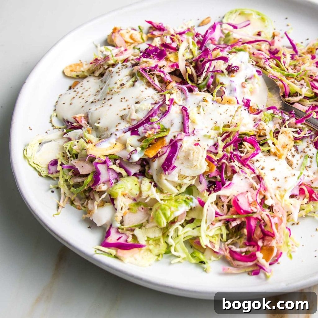 Shredded brussels sprouts and cabbage salad with creamy dairy-free dressing on a white plate, sprinkled with toasted nuts and seeds