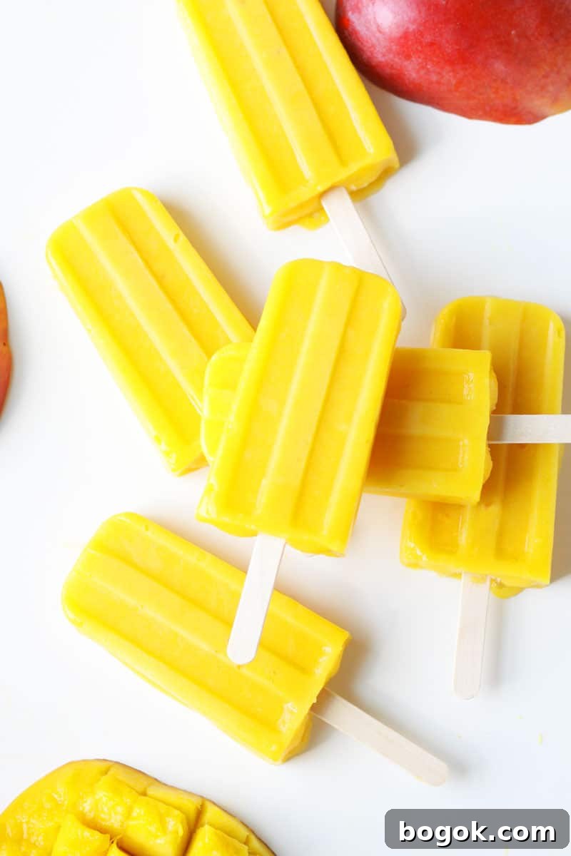 a pile of mango popsicles on a white tray with a sliced fresh mango behind them