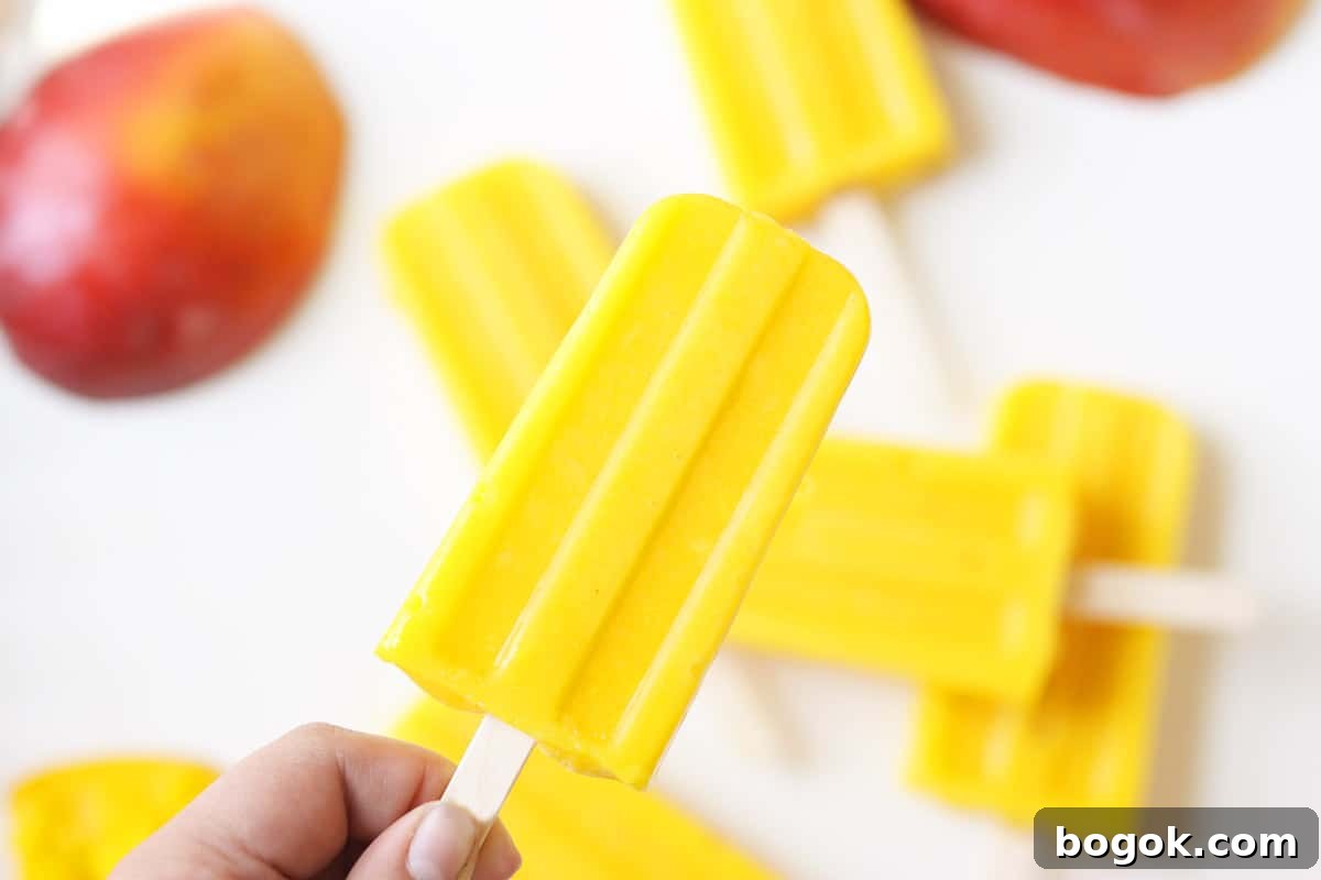 a pile of mango popsicles on a white tray with a sliced fresh mango behind them