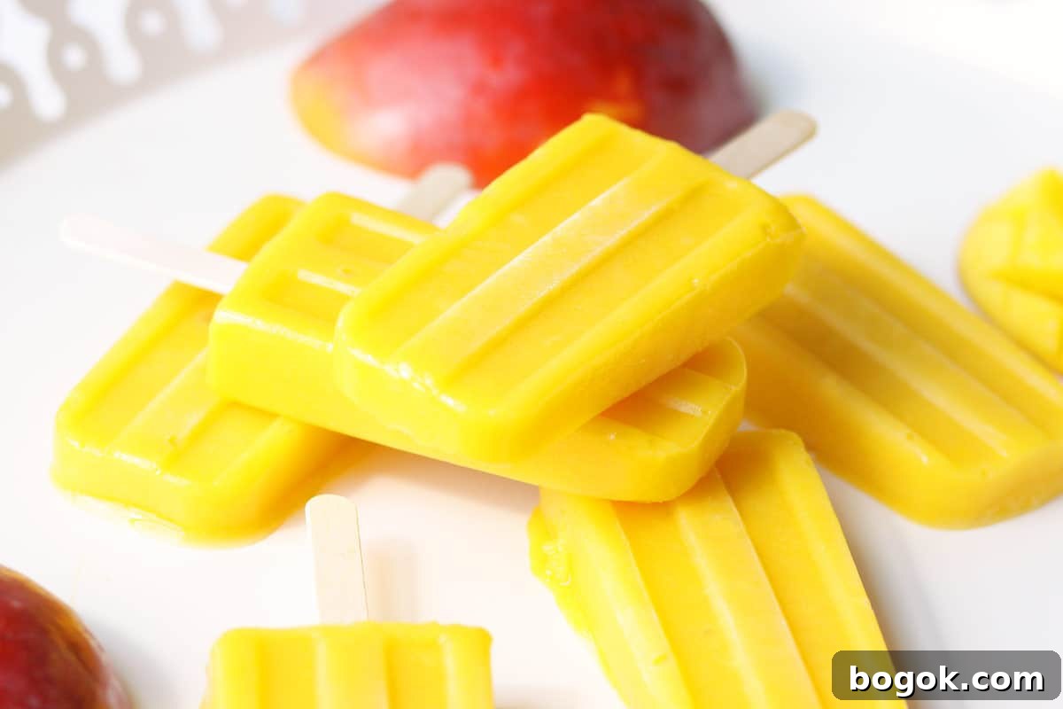 a pile of mango popsicles on a white tray with a sliced fresh mango behind them