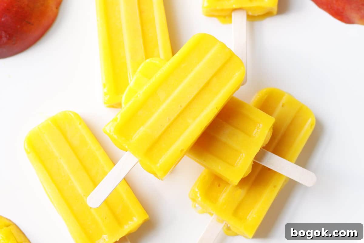 a pile of mango popsicles on a white tray with a sliced fresh mango behind them