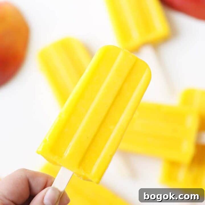 a pile of mango popsicles on a white tray with a sliced fresh mango behind them
