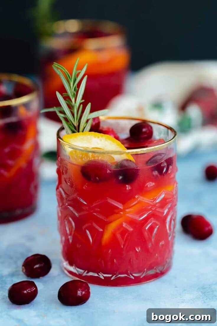 A cranberry orange margarita garnished with a fresh sprig of rosemary.
