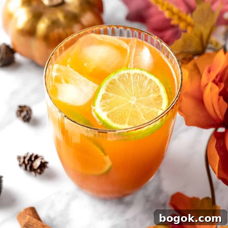 Overhead view of an orange pumpkin spice margarita, garnished with lime slices, next to an orange pumpkin.
