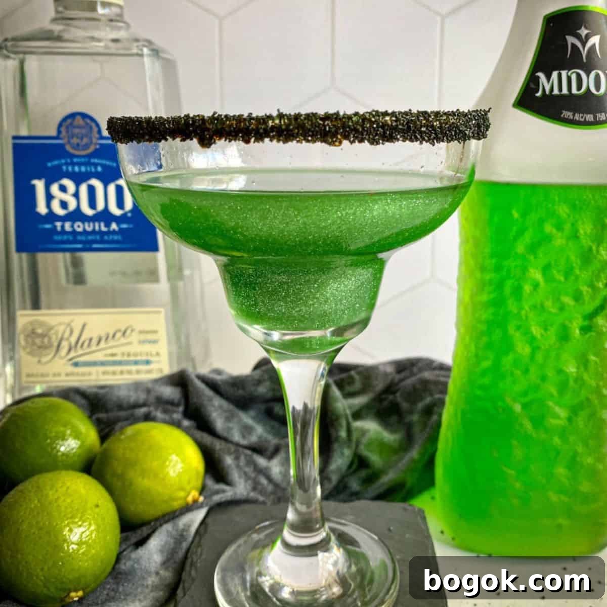 A green glittery Halloween margarita with a black sugar rim.