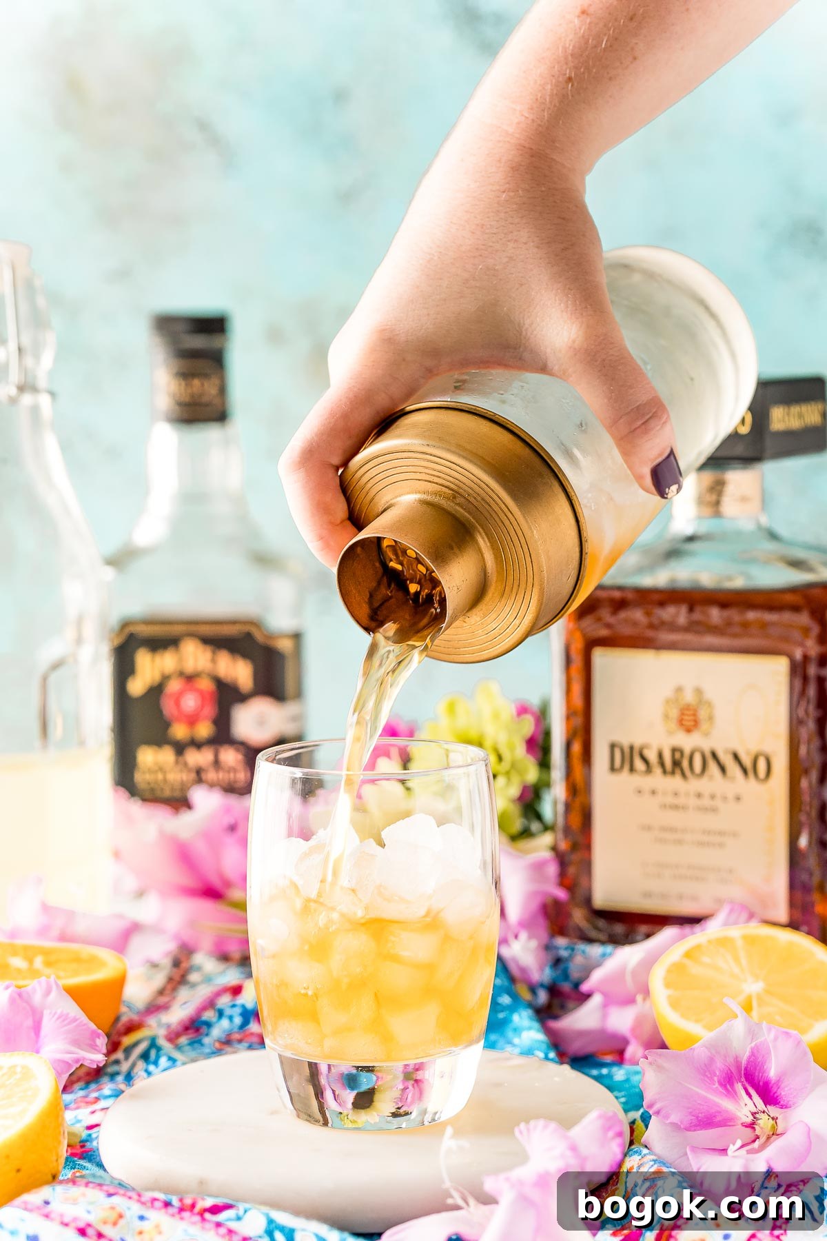Classic Amaretto Sour Cocktail Recipe with a Citrus Twist 9 A cocktail shaker pouring a drink into a rocks glass filled with ice.
