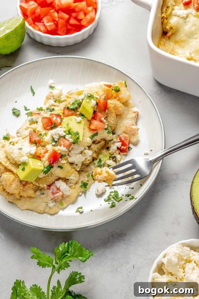 enchiladas topped with cheese, tomatoes and avocado on plate with fork