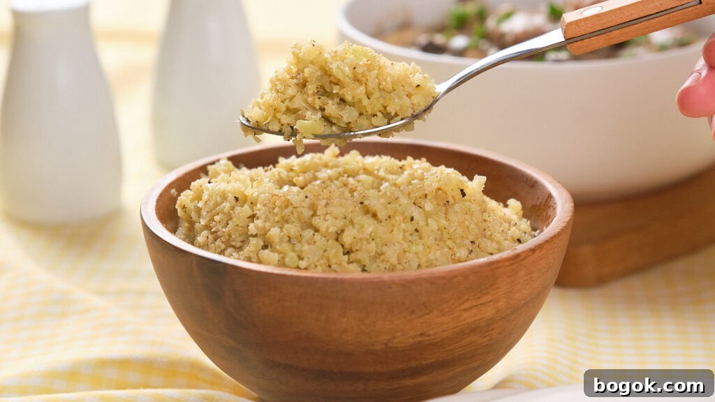 How to Make Cauliflower Rice at Home: Simple Step-by-Step Guide 4 A spoonful of cooked cauliflower rice hovers over a wooden bowl full of the same dish, with additional bowls in the background.
