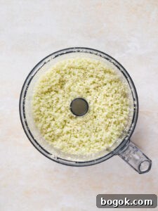 How to Make Cauliflower Rice at Home: Simple Step-by-Step Guide 7 Overhead view of chopped cauliflower pieces in a food processor on a light-colored surface.