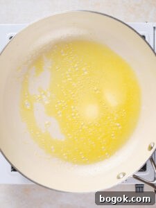 How to Make Cauliflower Rice at Home: Simple Step-by-Step Guide 8 A white skillet on a stovetop containing melted butter that is starting to bubble and foam.