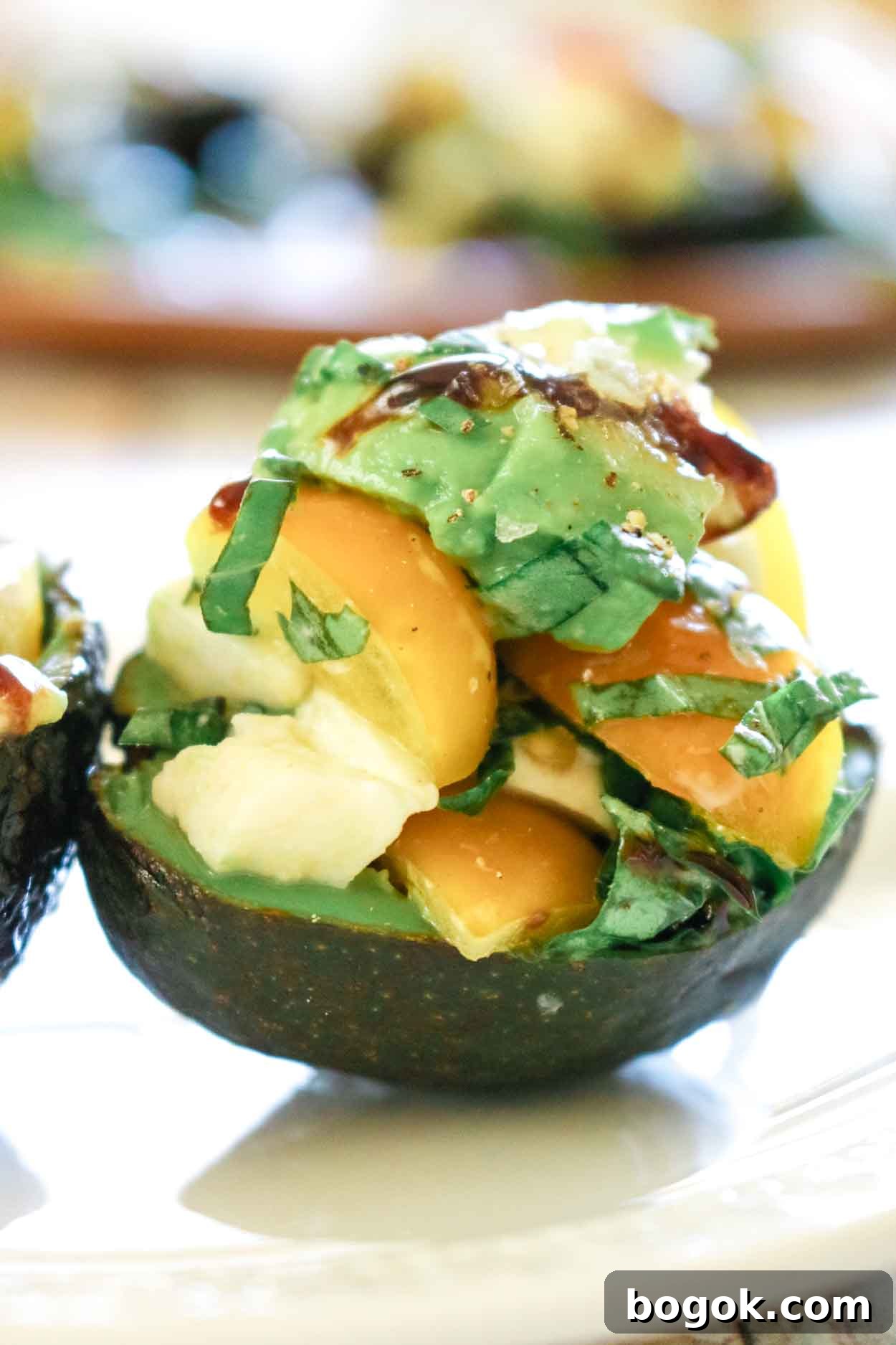 Caprese-Stuffed Avocados with 5 Ingredients 6 Avocado stuffed with caprese salad of mozzarella and tomatoes and drizzled with balsamic glaze on a white plate.