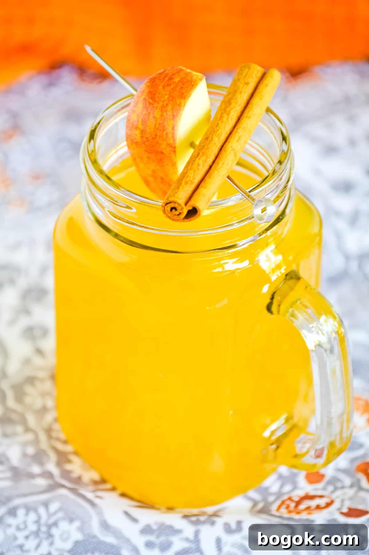Boozy hot apple cider in glass mason jar mug topped with skewer with fresh apple slice and a cinnamon stick