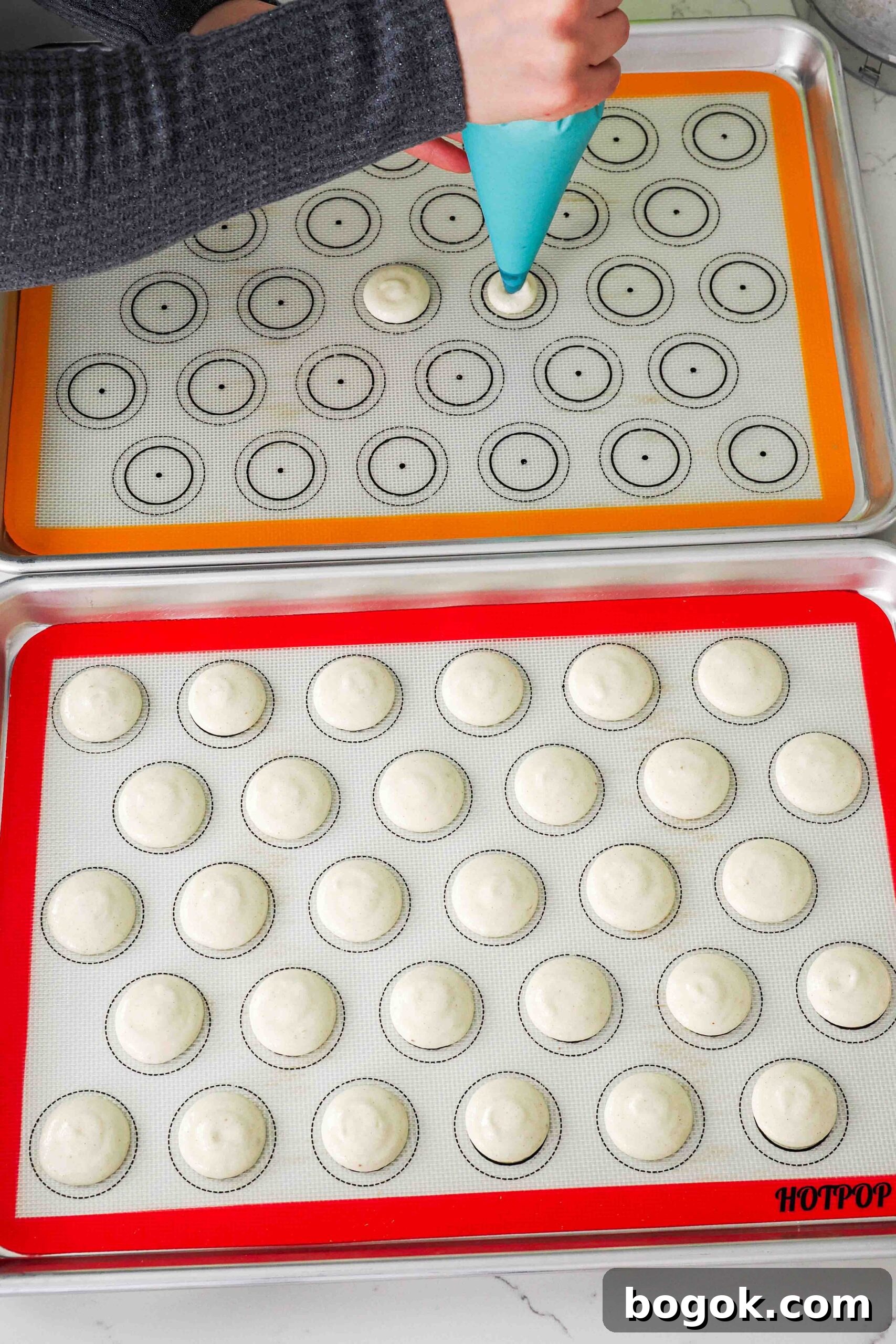 White Chocolate and Pomegranate Macarons — Recipe & Tips 11 A woman pipes macarons onto a silicone macaron mat.