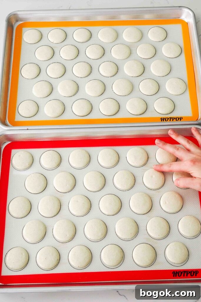 White Chocolate and Pomegranate Macarons — Recipe & Tips 12 A finger lightly touches a macaron shell to see if it has dried properly.