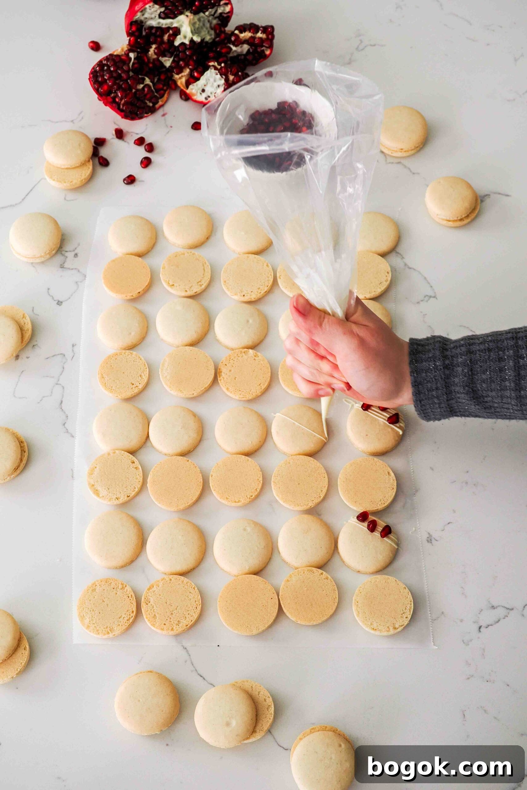 White Chocolate and Pomegranate Macarons — Recipe & Tips 16 A hand drizzles melted white chocolate over the top of a macaron shell.