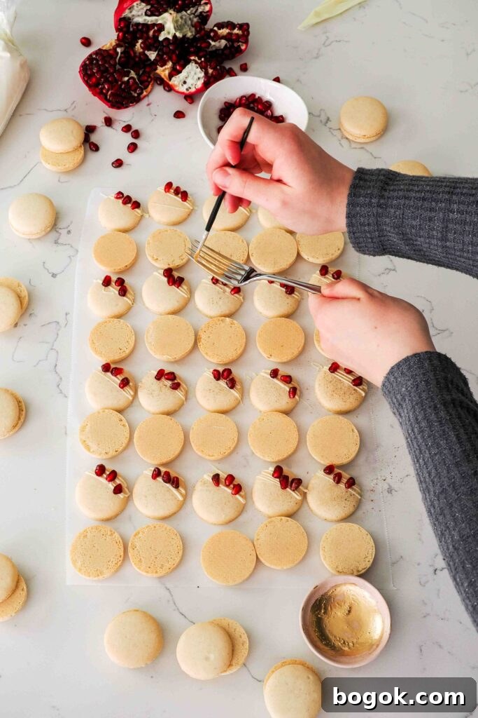 White Chocolate and Pomegranate Macarons — Recipe & Tips 17 A hand runs a paint brush over the tines of a fork to splatter macarons.