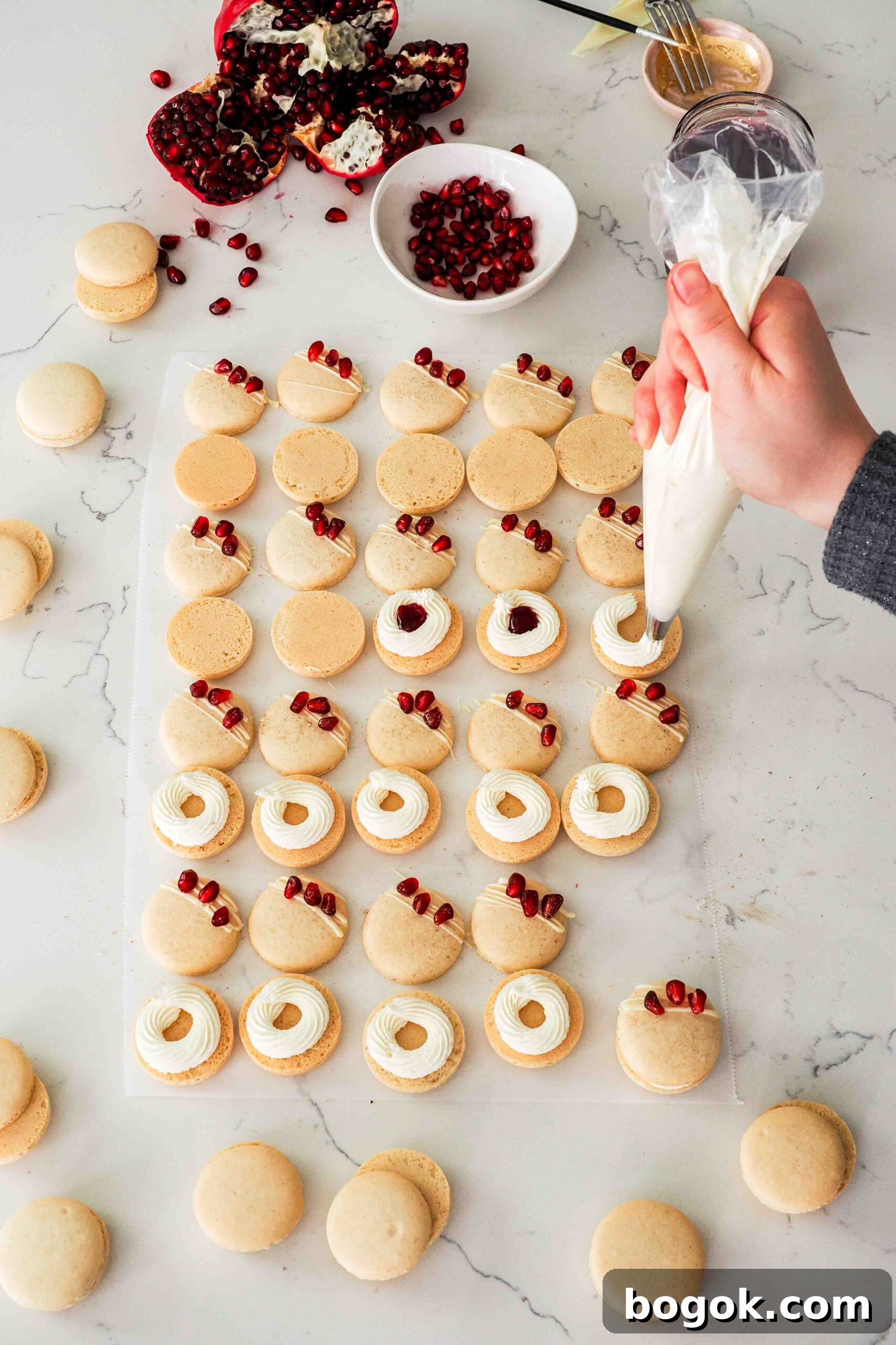 White Chocolate and Pomegranate Macarons — Recipe & Tips 18 A hand pipes a ring of white chocolate buttercream onto a macaron bottom.