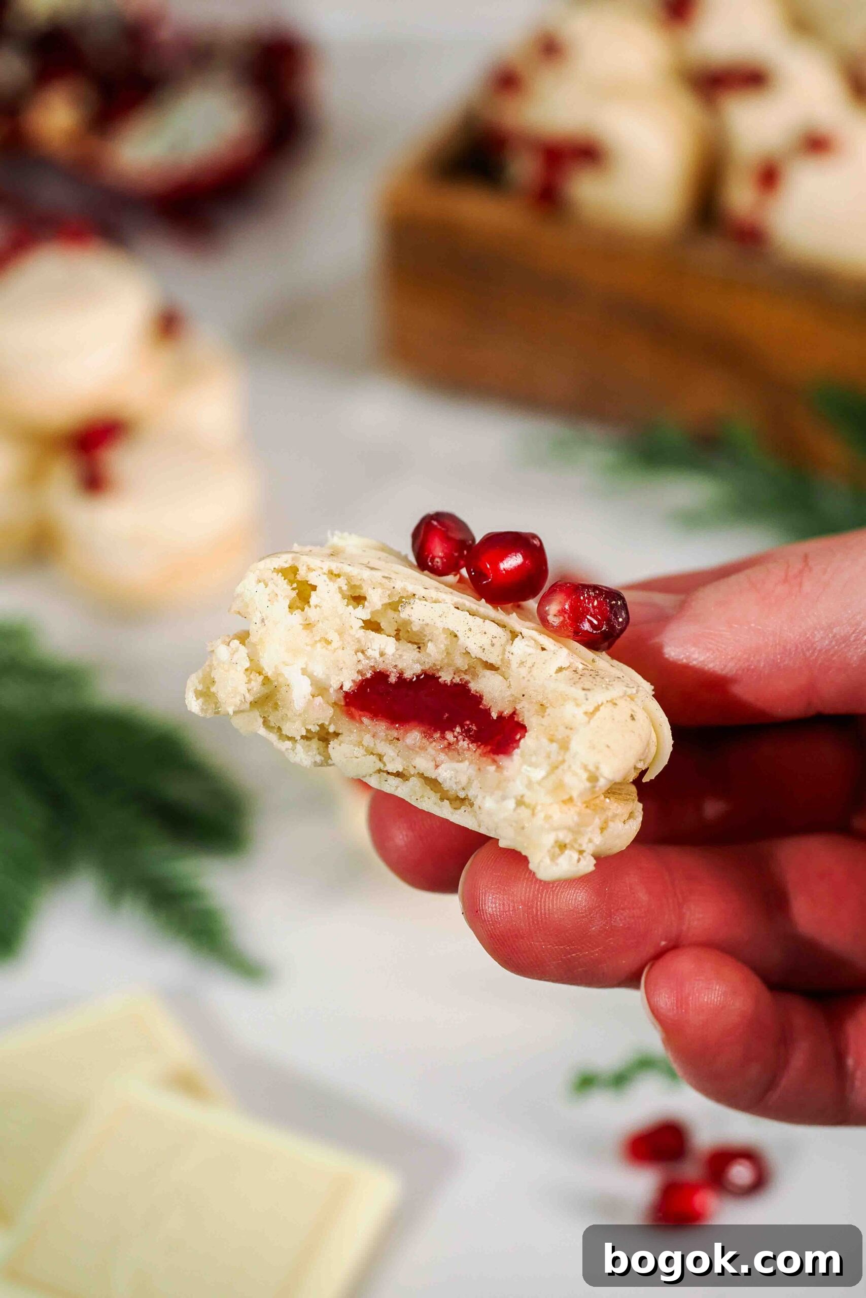 White Chocolate and Pomegranate Macarons — Recipe & Tips 4 A bite is missing from a white chocolate pomegranate macaron, showing the inside pomegranate jelly filling.