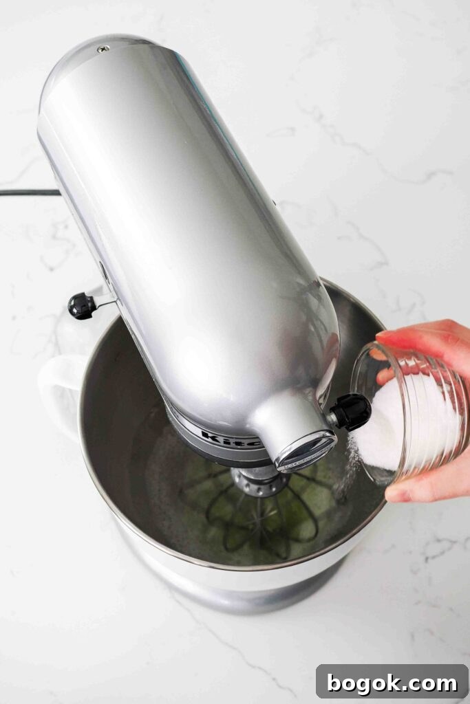White Chocolate and Pomegranate Macarons — Recipe & Tips 7 A hand sprinkles sugar into egg whites in a stand mixer.