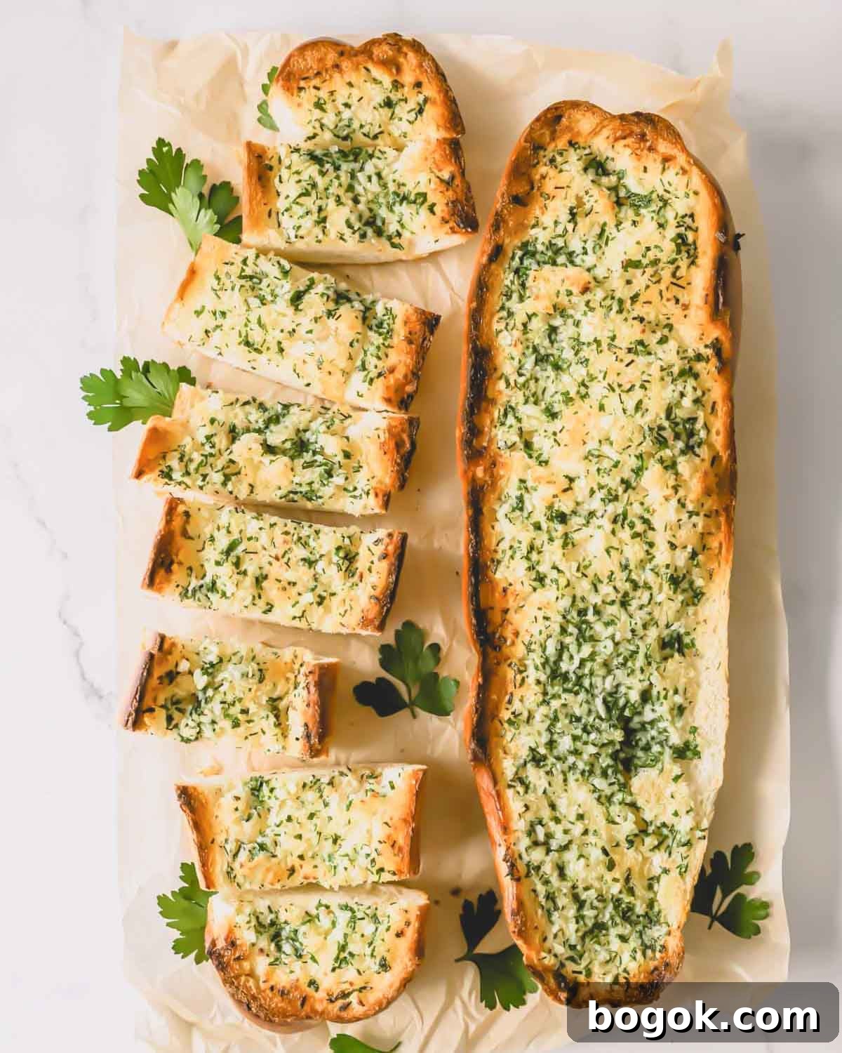 Garlic Bread Recipe with Crispy Herb Butter Crust 2 Two loaves of garlic bread topped with an herbed butter spread with one sliced into pieces.