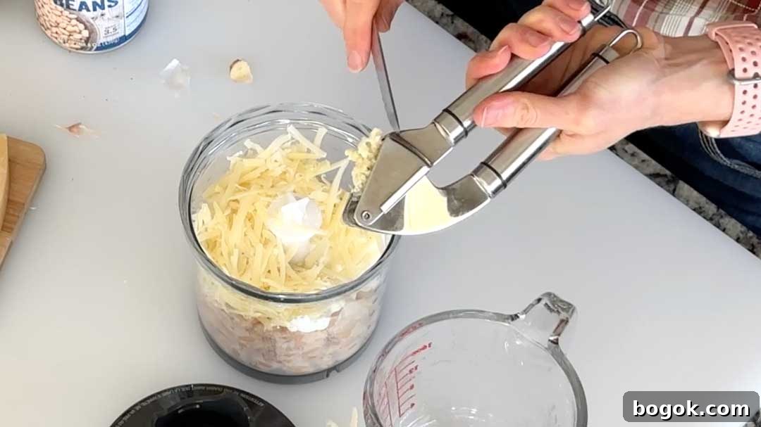 Garlic Parmesan White Bean Dip with Extra Protein 5 Adding minced garlic from a garlic press to a chopper cup for the white bean dip.