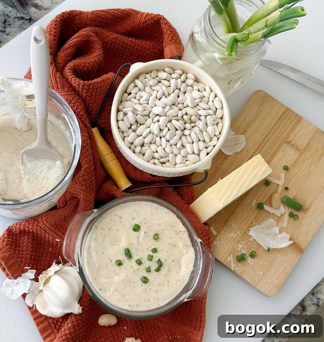 Garlic Parmesan White Bean Dip with Extra Protein 8 Glass bowl of white bean dip on an orange dish towel next to a bowl of white beans.