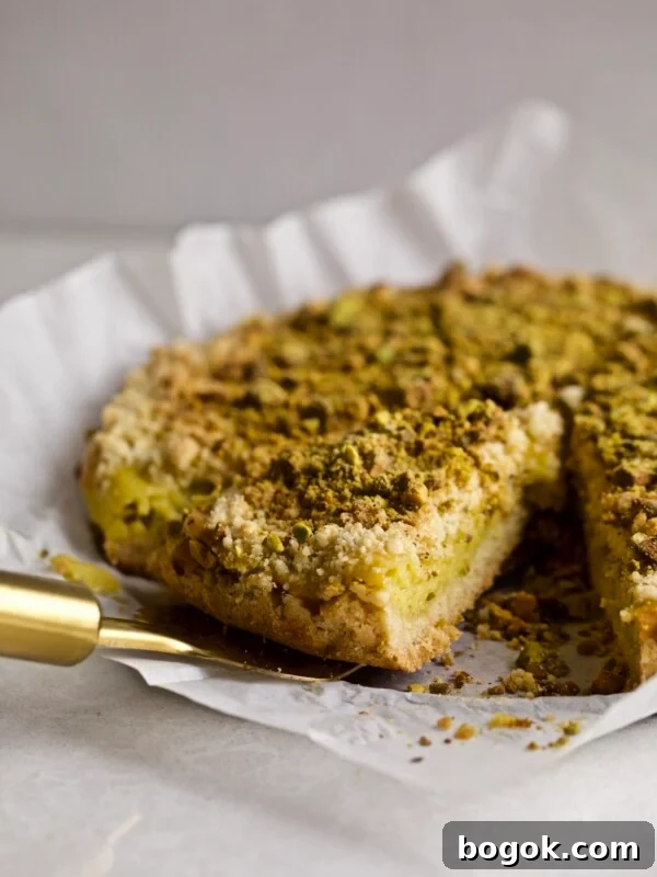 Italian Crumb Cake with Pistachio Cream (Sbriciolata) on a cake plate with a slice taken out with a pie server. Side angle shot.