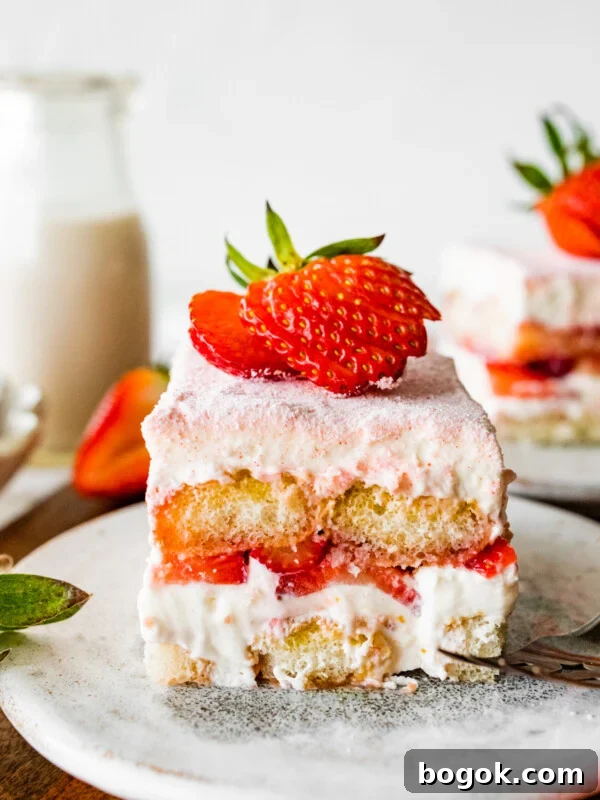 Single slice of the strawberry tiramisu on a plate with a sliced strawberry on top on a plate.