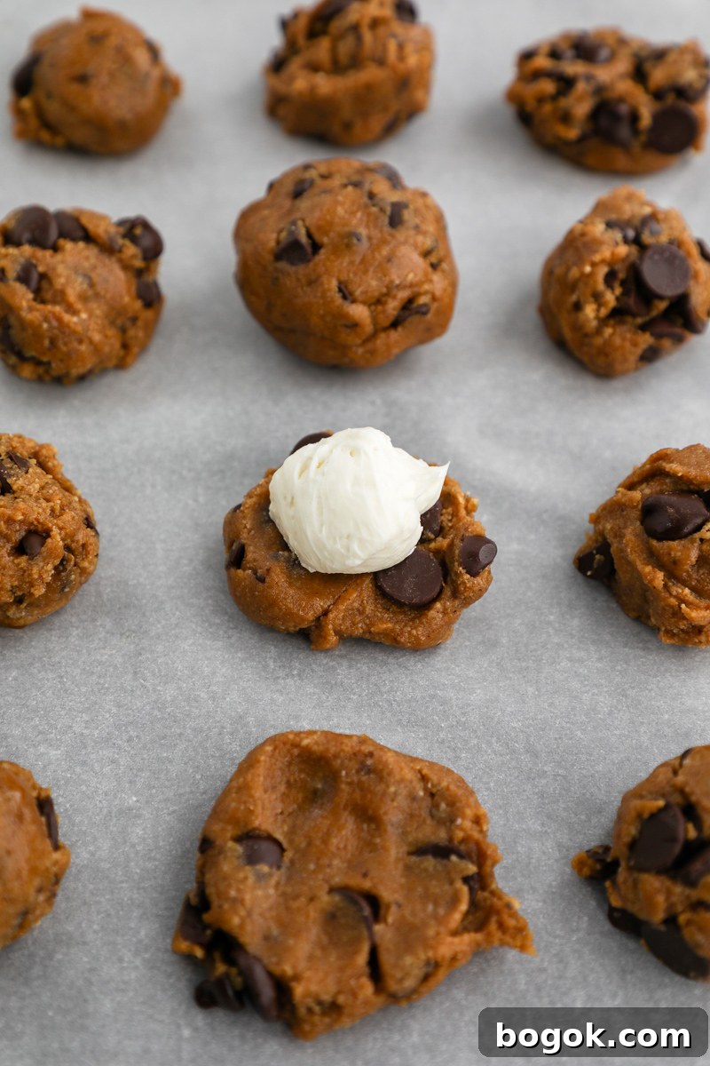 Balls of almond butter chocolate chip cookie dough sitting on a baking sheet showing the process of how to stuff your cookies with cream cheese filling