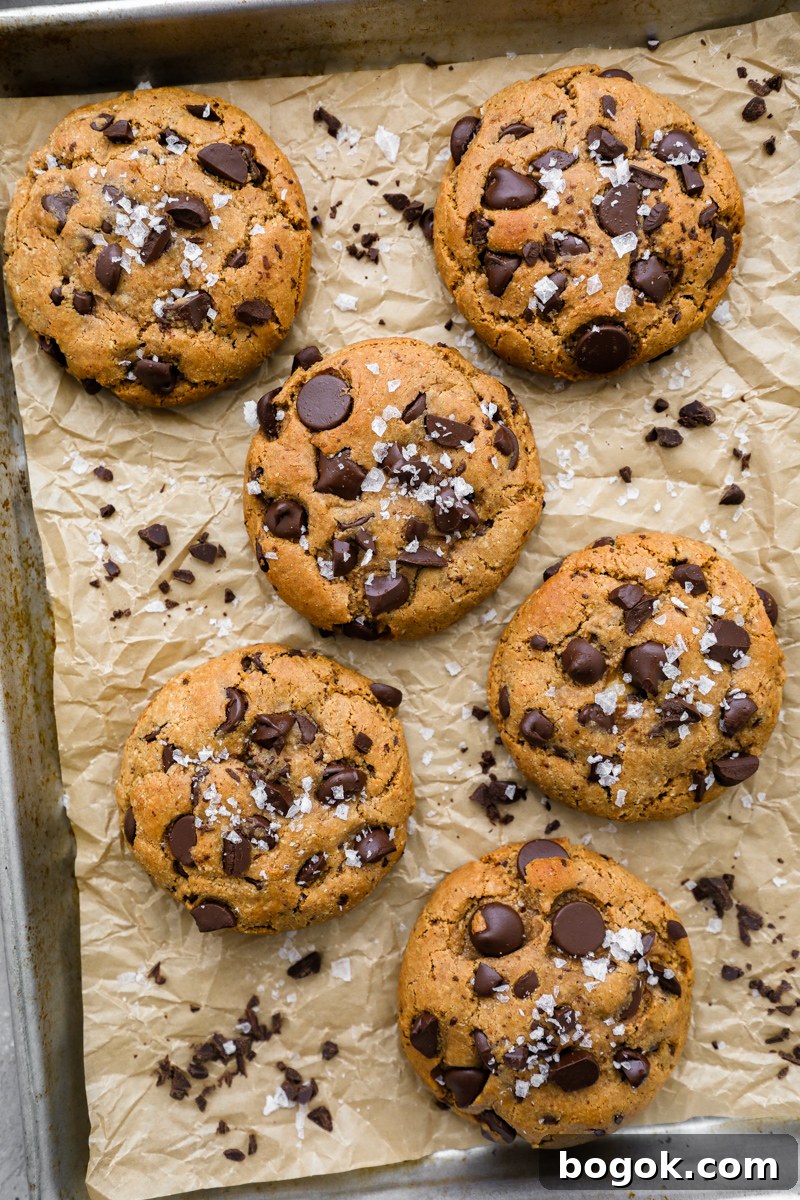 6 cheesecake stuffed cookies sitting on a baking pan lined with parhment paper with flakey sea salt sprinkled over the top