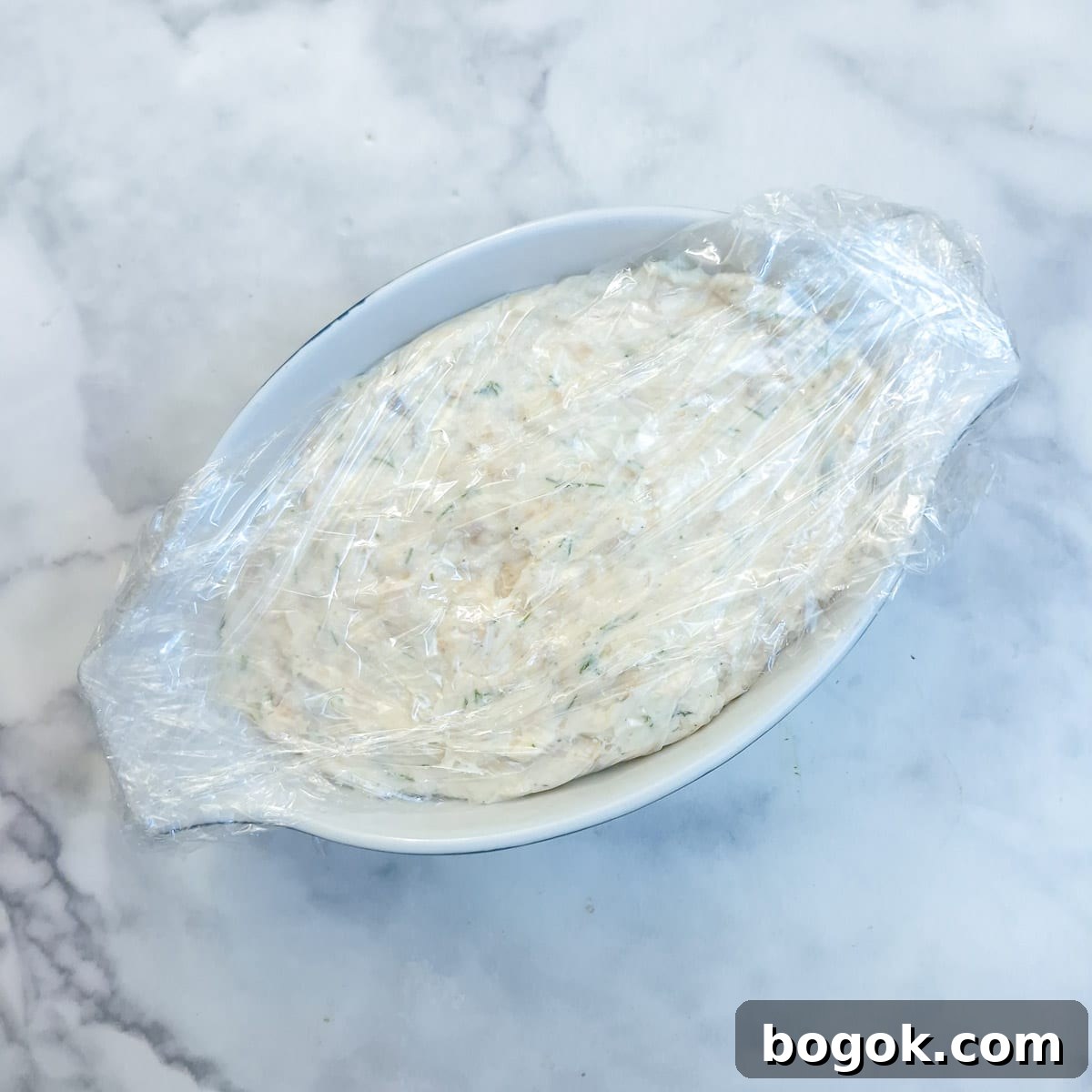 Salmon terrine in a white dish, wrapped in clingfilm.