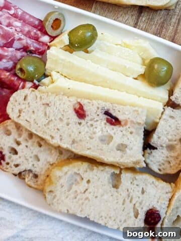 Slices of chestnut and cranberry focaccia on a long white plate with salami, cheese and olives.