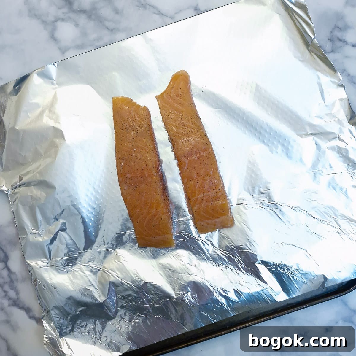 Two pieces of raw salmon on a sheet of tin foil on a baking tray.