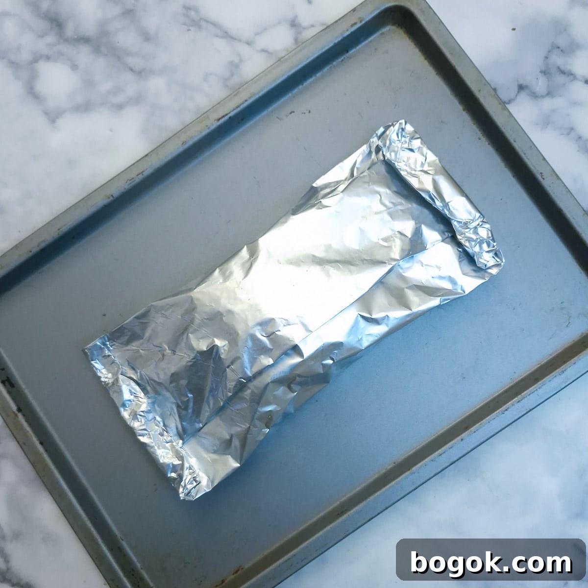 A foil-wrapped parcel of salmon ready to go into the oven on a baking tray.