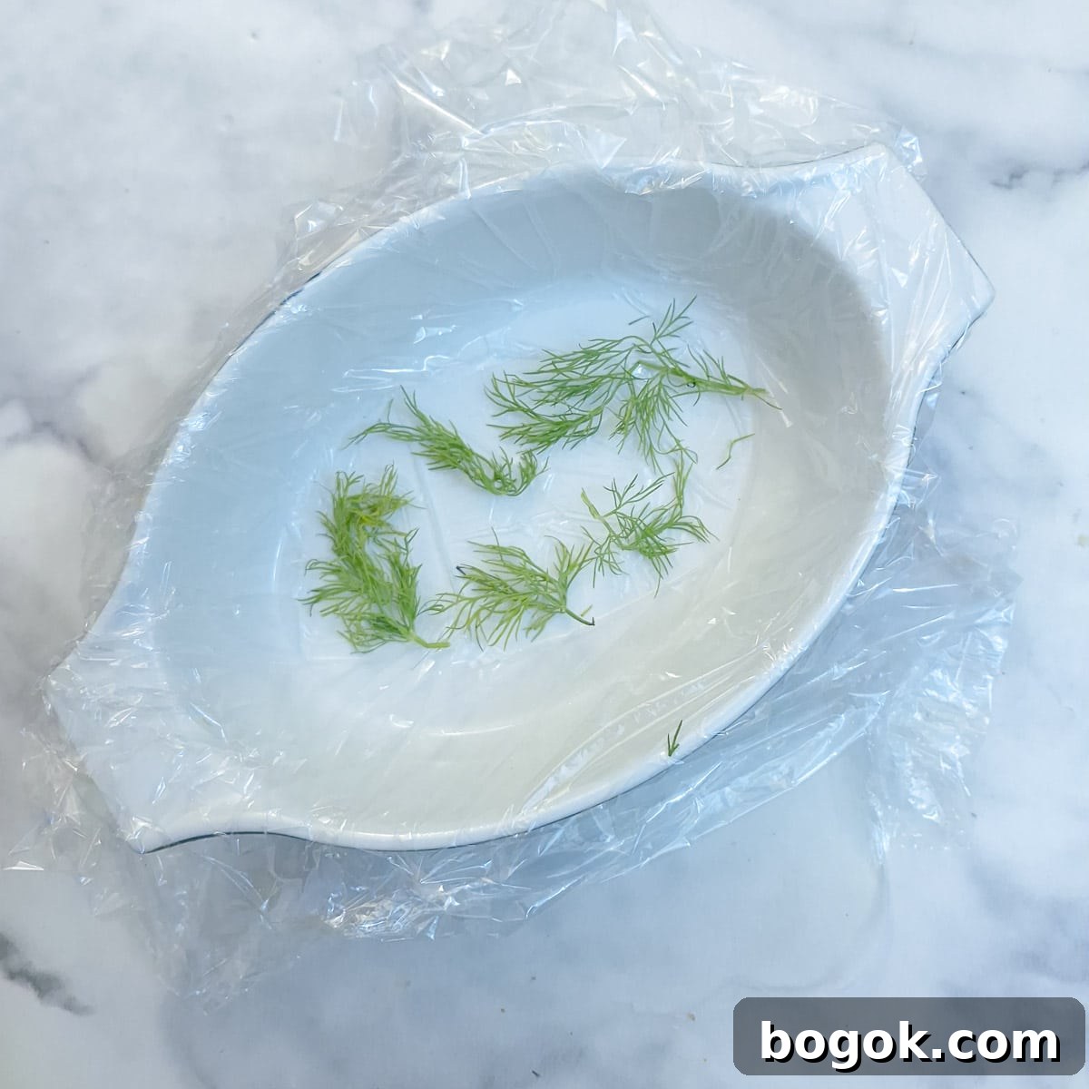 A small white dish, lined with clingfilm with a few sprigs of fresh dill on the bottom.