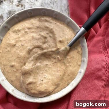 A bowl of remoulade sauce with a spoon and a pink towel.