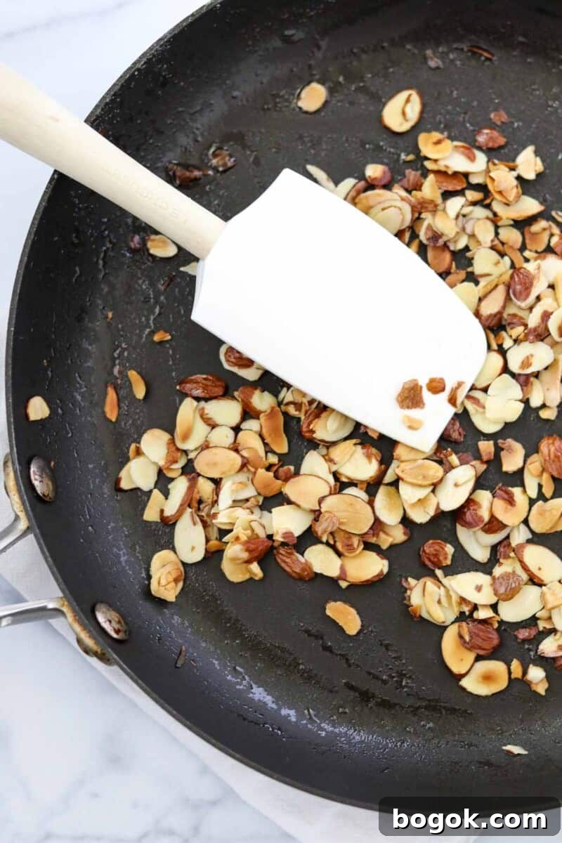 Swedish Tomato and Goat Cheese Salad with Herb Marinade 5 Toasted almonds in a skillet with a white rubber spatula.