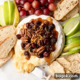 A round wheel of baked brie cheese with a fruit and nut topping, with apples, pears, and crostini.