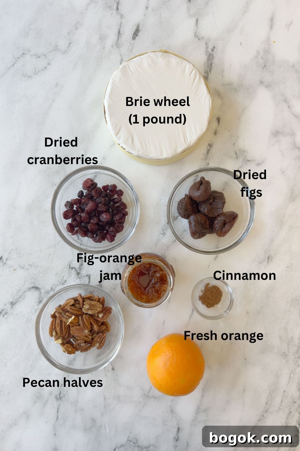 Ingredients for baked brie cheese appetizer on the counter with cranberries, figs, pecan, jam, orange, and cinnamon.